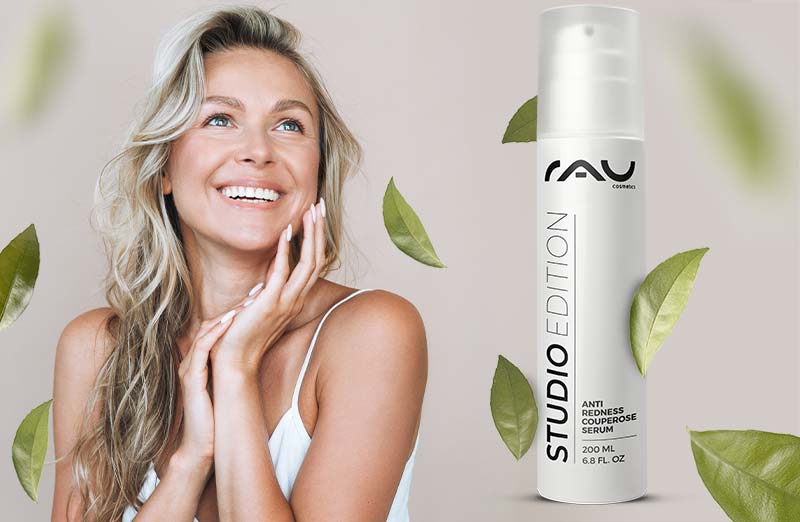 Lächelnde Frau mit langem, welligem Haar hält Anti-Rötung Serum von RAU Cosmetics vor grünen Blättern.