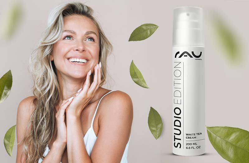 Frau mit gesunder Haut präsentiert RAU Cosmetics White Tea Cream neben grünen Blättern, Inhalt und Frische betonend.