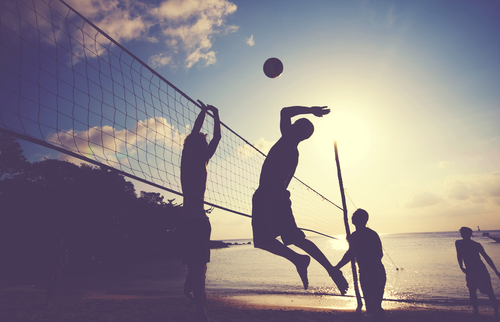 beacher-tipps-profi-volleyball-beachvolleyball-rau-cosmetics Silhouetten von Beachvolleyballspielern, die vor dem Hintergrund eines Sonnenuntergangs springen und einen Ball schmettern, was Outdoor-Sport und Sonneneinstrahlung betont.