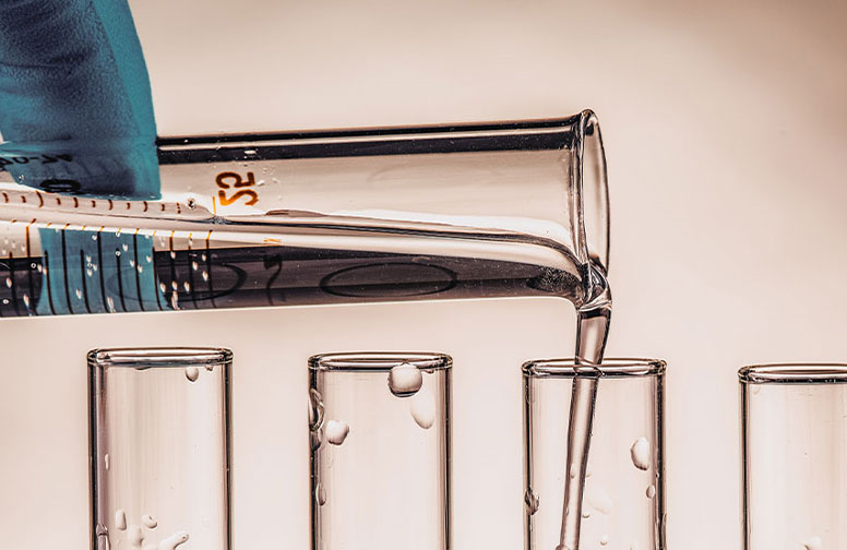 RAU_Cosmetics_kolloidales-silber-92 Glasbehälter mit Flüssigkeit wird in mehrere Reagenzgläser gegossen, symbolisiert die Herstellung von kolloidalem Silber für die Hautpflege.