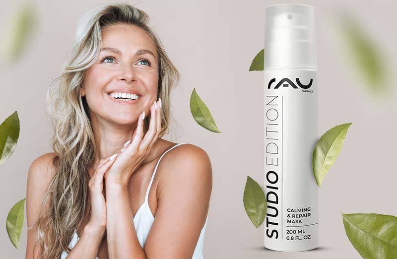 Lächelnde Frau mit RAV Calming & Repair Maske, umgeben von grünen Blättern für natürliche Hautpflege.