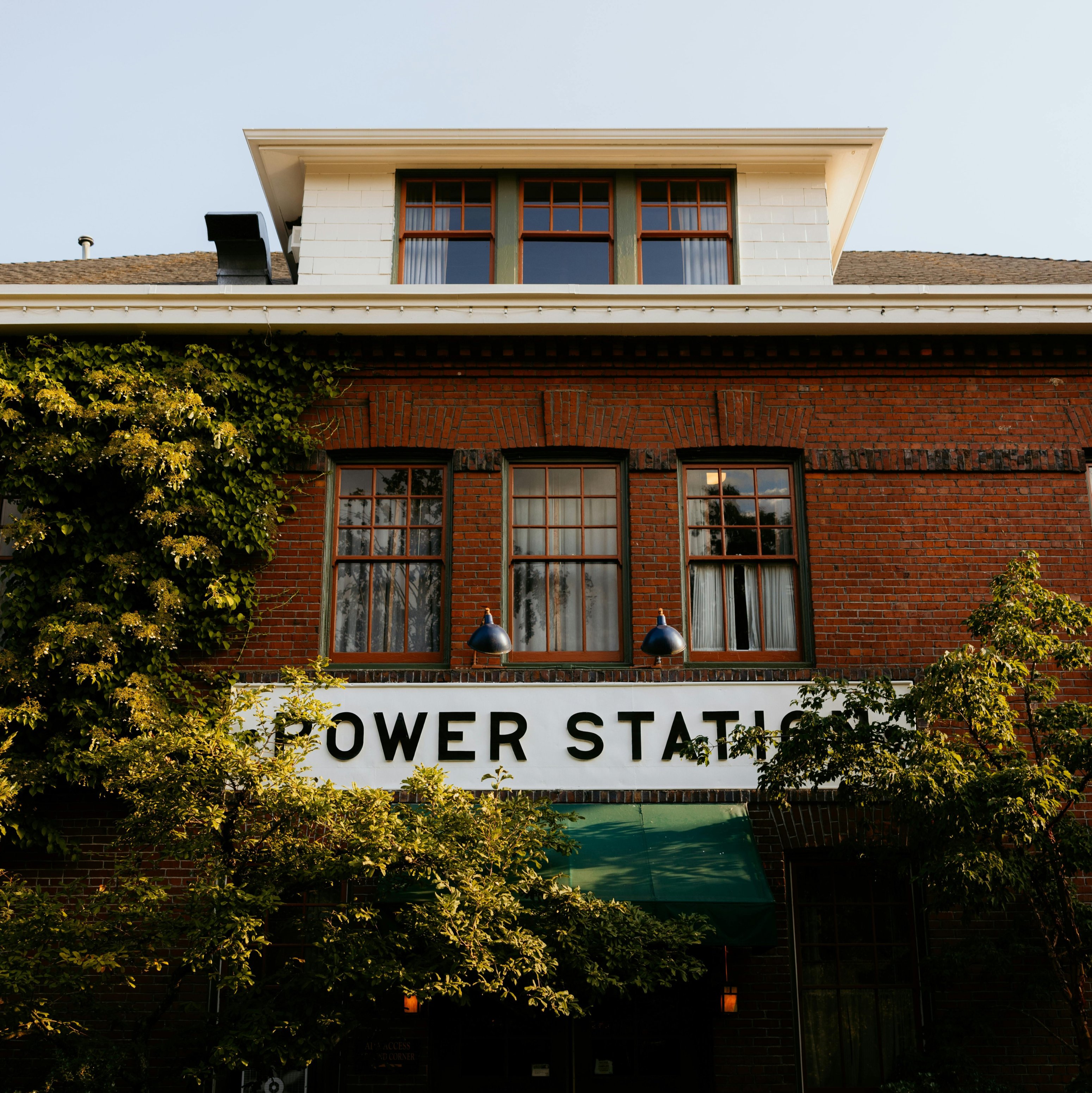 Gebäude mit der Aufschrift "POWER STATION", umgeben von Pflanzen und Fenstern, im Kontext von Wellness und Energieproduktion.
