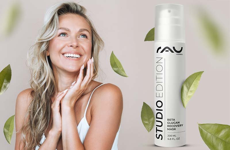 Frau mit fröhlichem Gesicht verwendet Beta Glucan Recovery Mask von RAU Cosmetics, umgeben von grünen Blättern.