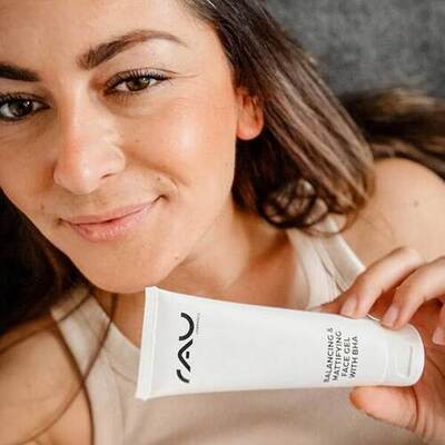 Frau mit entspannter Miene hält "Balancing & Hydrating Face Cream mit SPF" von RAU Cosmetics.